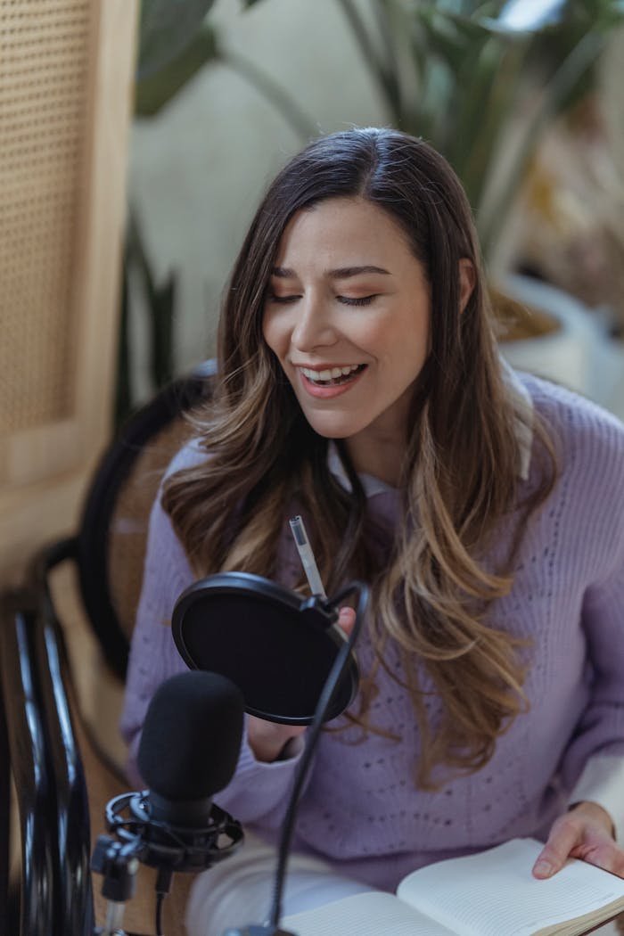 services-03 Positive female radio host with professional microphone sitting on chair while recording audio message in light room with green plants